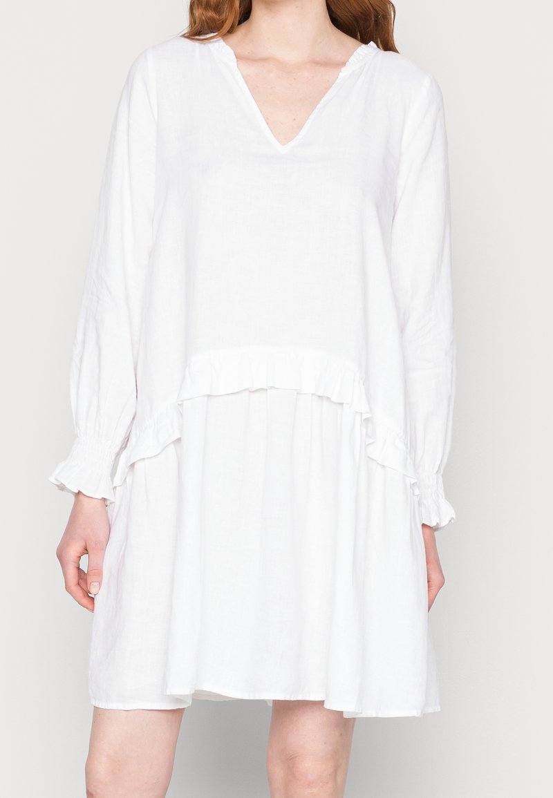Vestido de lino blanco con escote en V, mangas largas con puños con volantes y un diseño en capas con un detalle de volante en la cintura.
