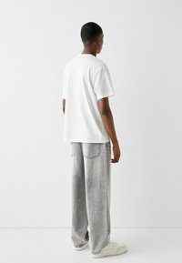 Witte t-shirt met korte mouwen, gecombineerd met losse grijze denim broek met een relaxed fit, achterzakken en neutrale sneakers.