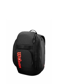 Sac à dos noir avec texture géométrique, poche zippée avant et logo "Wilson" rouge bien en vue. Dispose d'une poignée supérieure et de bretelles ajustables.