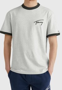 Grå bomull T-shirt med svart ribbad halsringning och ärmar, med en svart textlogo på bröstet. Tyget har en mjuk textur.