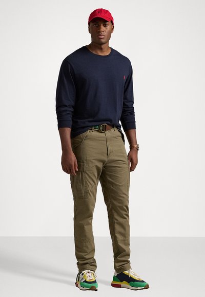 Marineblauwe longsleeve shirt, olijfgroene cargobroek, rode pet, multicolour sneakers met gele veters. Contrasterende stiksels en zakken op de broek.