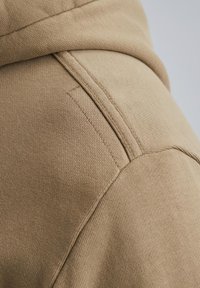 Beige hoodie van een soepele katoenmix, met een gebogen capuchon en gedetailleerde stiksels langs de schoudernaad.