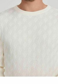 Kremowy sweter dziany z teksturowanym wzorem warkocza, okrągłym dekoltem i ściągaczami na mankietach. Tkanina ma miękki, lekki wygląd.