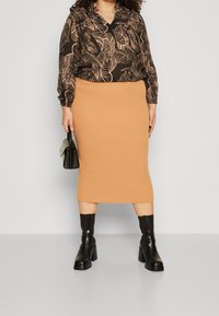 Svart blus med beige lövmönster, kombinerad med en ribbad ljusbrun midikjol. Modellen bär knähöga svarta stövlar och håller en liten svart väska.