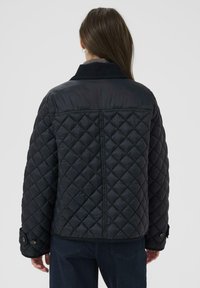 Black quilted jacket featuring a corduroy collar, snap buttons on cuffs, and textured fabric. Back view shows diamond pattern and seams.