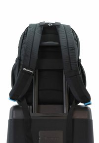 Mochila negra con correas acolchadas, respaldo de malla, unida a una maleta rodante negra. Presenta un logotipo y un acento azul en las correas.