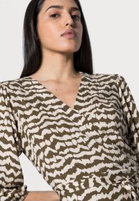 Vestido envelopado em verde oliva com padrão abstrato em creme; apresenta um decote em V profundo e mangas franzidas; feito de tecido leve.