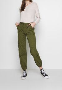 Olivgrön cargobyxor med elastiska muddar och sidofickor, matchade med en ljusbeige tröja. Bärs med svarta högskurna sneakers.