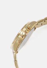 Montre-bracelet dorée avec un boîtier rond, trois boutons latéraux et un bracelet maillon. Surface lisse avec une finition réfléchissante.