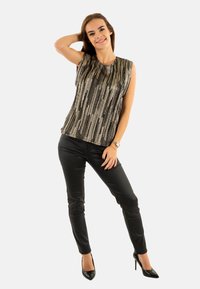 Top sin mangas con un patrón de rayas verticales en negro y plateado, hecho de una tela ligera. Combinado con pantalones negros ajustados y tacones altos.