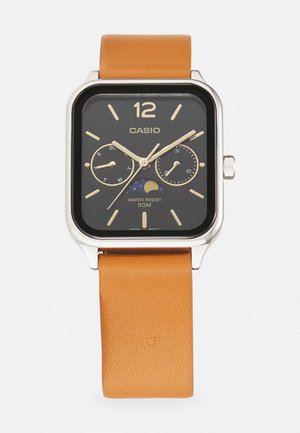 Casio laikrodis su kvadratiniu juodu ciferblatu, auksiniais akcentais ir baltais rodyklėmis. Jis turi rudą odinę apyrankę ir yra atsparus vandeniui iki 50 m.