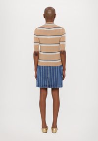 Haut en tricot rayé beige à manches courtes associé à une jupe en jean bleue avec des coutures blanches verticales. Chaussures à enfiler texturées dorées.