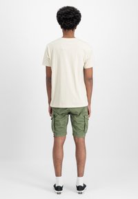 Beež puuvillane t-särk lühikeste varrukatega, koos oliivroheliste cargo-lühikesed pükstega, millel on külje taskud, valged sokid ja mustad tennisetossud.