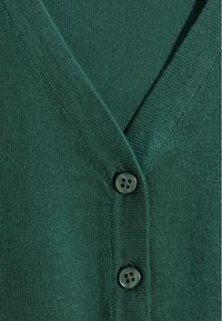 Groene gebreide cardigan met een V-hals, twee donkere knopen en een zachte textuur. Focus op het breimuster en het naadloze ontwerp.