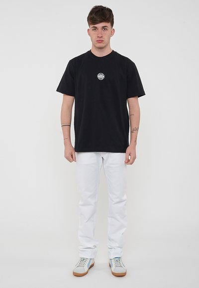 Camiseta de algodón negra con un logo redondo en el pecho, combinada con jeans de mezclilla blancos y zapatillas con acentos azul claro. Diseño simple, corte relajado.