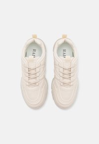 Beige sneaker with a smooth leather upper, lace-up design, padded collar, and a textured rubber sole. Features a looped heel tab.