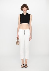 Top nero a maniche corte con bordi a scallop, pantaloni bianchi a vita alta con chiusura a cinque bottoni, sandali neri con cinturini e borsa a tracolla con motivo.