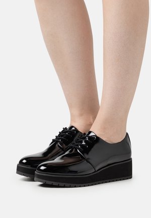 Schwarze Lacklederschuhe mit einem eleganten Design, das eine abgerundete Spitze, eine dicke schwarze Plateausohle und schwarze Schnürsenkel umfasst.