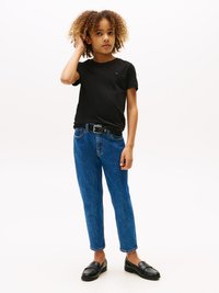 T-shirt noir à manches courtes, jean en denim bleu délavé avec une coupe slim, ceinture noire et mocassins noirs. Enfant se tenant debout de manière décontractée, main sur la tête.