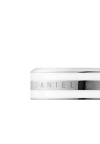 Valkoinen kello, jossa on sileä, pyöristetty keramiikkakotelo, hopeiset yksityiskohdat ja metallinauhassa kaiverrettu "DANIEL WELLINGTON". Minimalistinen muotoilu.