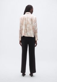 Světlá růžová halenka s květinovým vzorem a dlouhými rukávy, v kombinaci s černými širokými kalhotami s vysokým pasem a botami na podpatku.