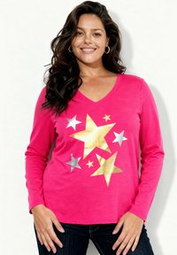 Różowa koszula z długim rękawem i dekoltem w serek ozdobiona dużymi wzorami gwiazd w kolorze złotym i srebrnym. Miękki materiał, luźny krój, zestawiona z ciemnymi dżinsami.