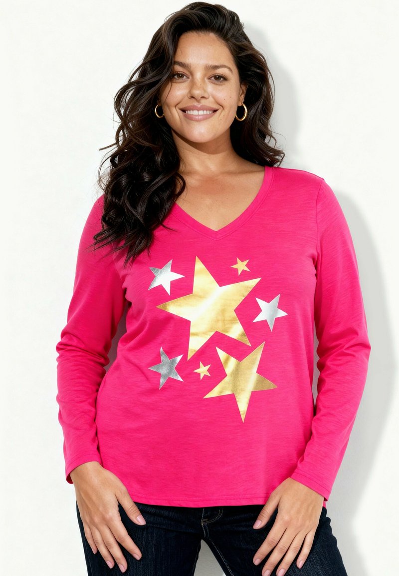 Różowa koszula z długim rękawem i dekoltem w serek ozdobiona dużymi wzorami gwiazd w kolorze złotym i srebrnym. Miękki materiał, luźny krój, zestawiona z ciemnymi dżinsami.