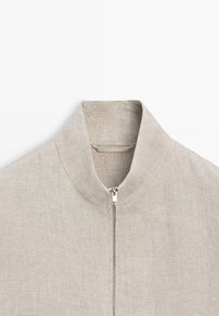 Light beige textured fabric jacket with a stand-up collar and a front silver zipper closure.