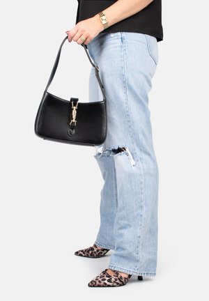 Borsa a tracolla in pelle nera con forma curvata e hardware dorato, tenuta in una mano. Sono visibili jeans blue strappati e scarpe con punta a forma di leopardo.