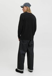 Black knit sweater, loose dark blue jeans with rolled cuffs, and a gray cap. The outfit has minimalistic design with no visible logos.