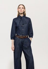 Dark denim blouse with a bow tie collar, featuring gold buttons. Paired with wide-leg trousers and a brown belt with decorative hardware.