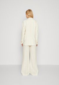 Lichtgekleurde, gestreepte pak met brede pijpen en een getailleerde blazer met knoopaccenten. Het materiaal lijkt lichtgewicht en textuur te hebben.