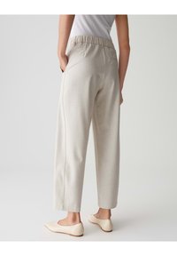 Helle beige, strukturierte Hose mit lockerem Schnitt, elastischem Bund, seitlichen Taschen und geraden Beinen. Kombiniert mit hellen Ballerinas.