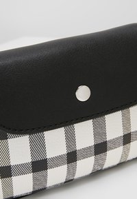 Clutch in finta pelle nera con un motivo a scacchi bianco e nero. Dotato di chiusura a scatto argentata e superficie liscia.