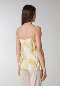 Top sin mangas en amarillo claro y blanco con un patrón abstracto y fluido. Hecho de una tela suave con tirantes finos ajustables.