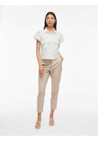 Witte overhemd met korte mouwen, knopen aan de voorkant en twee borstzakken, gecombineerd met lichtbeige slanke broek en doorzichtige sandaaltjes met hak.