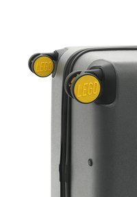 Gray suitcase with a textured finish features large yellow LEGO-branded wheels, black hardware, and a zippered closure.