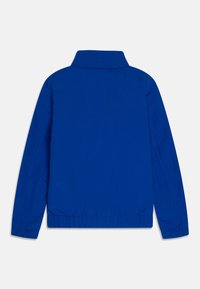 Giacca leggera blu con colletto, polsini e orlo elasticizzati. Tessuto liscio con dettagli di cucitura minimi sul retro.