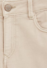 Bež denim tkanina s glatkom teksturom, s vidljivim džepom i gumbom s utisnutim natpisom "Blue Ridge." Čiste šavove i minimalno detaljiranje.