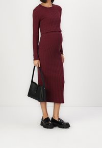 Burgundská nařasená pletená cropped top se sladěnou midi sukní. Černá kožená kabelka a robustní černé mokasíny dotvářejí vzhled.