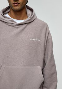 Lichtgrijze hoodie met een gestructureerde afwerking, voorzien van een voorzak en "Eternity Project" geborduurd in het wit.