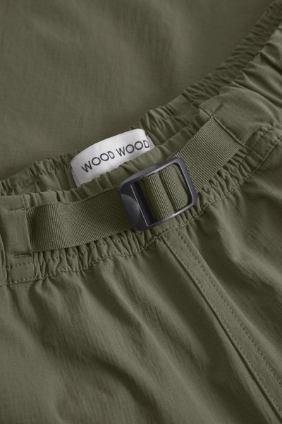 Olivgröna shorts med resårmidja, som har ett platt spänne och en etikett märkt "WOOD WOOD." Slät yta och enkel design.