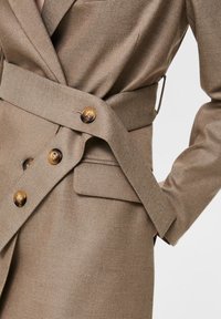 Beige op maat gemaakte blazer van een gestructureerde stof, met een dubbelknoopsluiting, opvallende knopen, een wikkelriem en een slim fit.