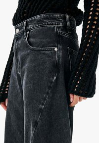 Jeans in denim nero a vita alta con effetto sbiadito, tasca frontale e dettagli in metallo argentato. Abbinati a un top nero in crochet dalla texture.