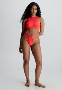 Ljusa orange Calvin Klein-bh med hög hals och nyckelhålssömmar, i kombination med matchande stringtrosor med logoband och minimal täckning.