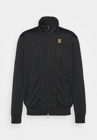 Svart zip-up jacka med hög krage, försedd med horisontella sömmar och sidofickor; inkluderar en liten, färgglad logotyp på bröstet.