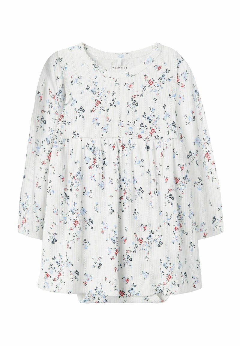 Un haut à manches longues blanc présente un motif floral avec des accents bleus et rouges, un tissu texturé et une taille froncée pour un ajustement ample.