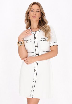 Witte jurk met korte mouwen, zwarte stikaccenten, decoratieve knopen en twee voorzakken. Vlotte textuur met een getailleerd ontwerp.