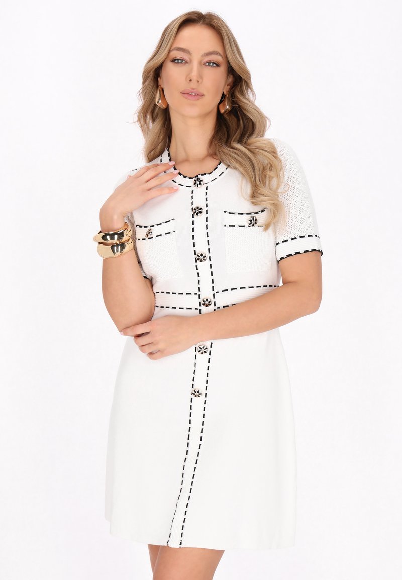 Weißes Kleid mit kurzen Ärmeln, schwarzen Nähakzenten, dekorativen Knöpfen und zwei Fronttaschen. Glatte Textur mit taillierter Passform.