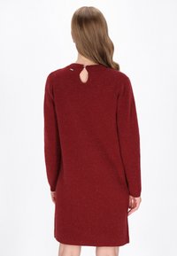 Vestido de punto rojo con mangas largas, cuello redondo y un pequeño detalle de ojo de cerradura en la espalda. Textura sutil con un aspecto ligeramente jaspeado.